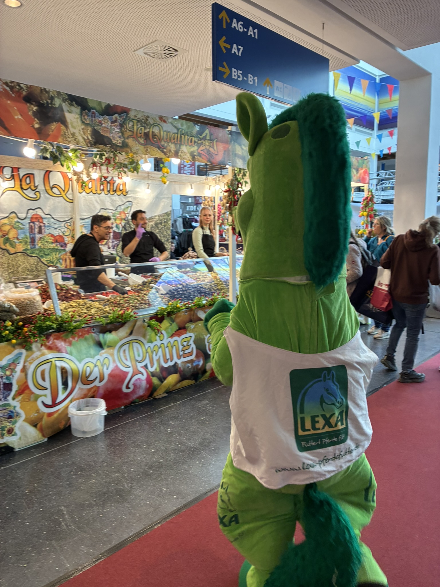 LEXA Maskottchen neben Reiterin auf Pferd im Außenbereich der Messe