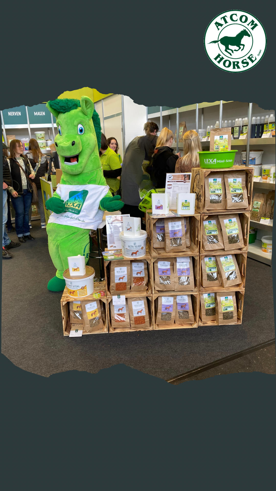 ATCOM Horse Messeauftritt mit Maskottchen Ein grünes Maskottchen in Form eines Pferdes steht neben einem Regal mit verschiedenen Produkten für Pferde. Im Hintergrund sind Menschen zu sehen.