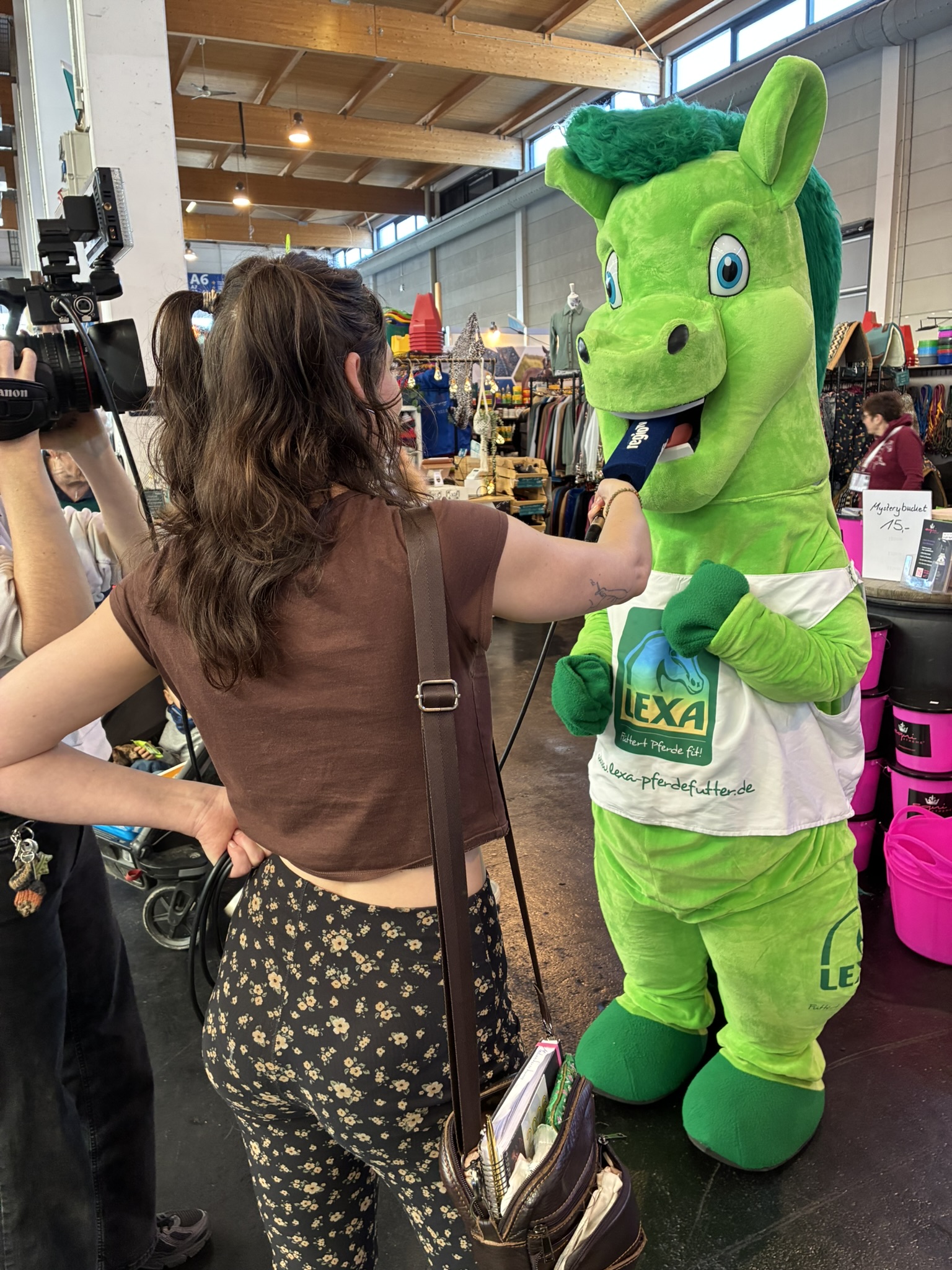 LEXA Maskottchen überreicht Produkte an Besucherin – Messeaktion mit Hund